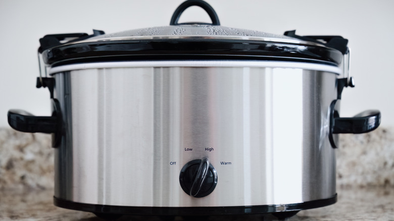 A stainless steel and black slow cooker set on high heat on a granite counter.