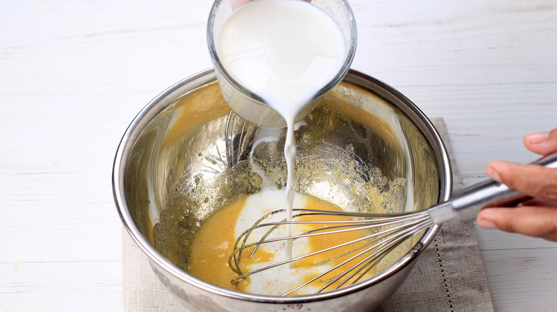 pouring milk into bowl with eggs