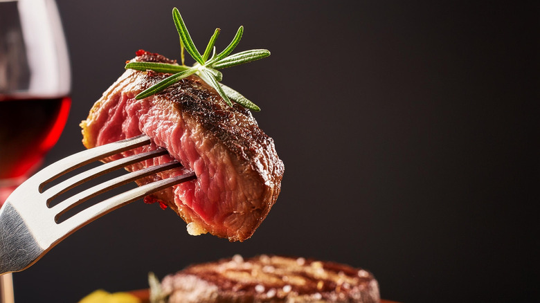 Fork holding bite of medium rare steak.