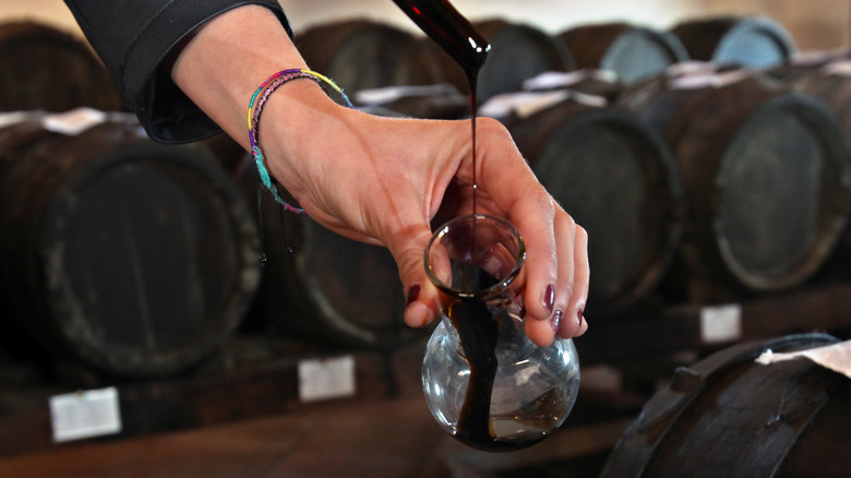 Person pouring balsamic vinegar from barrel into carafe