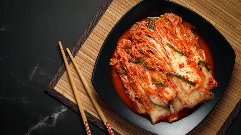 Fermented kimchi on a black plate with chopsticks