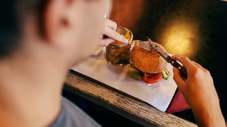 person cutting burger with cutlery