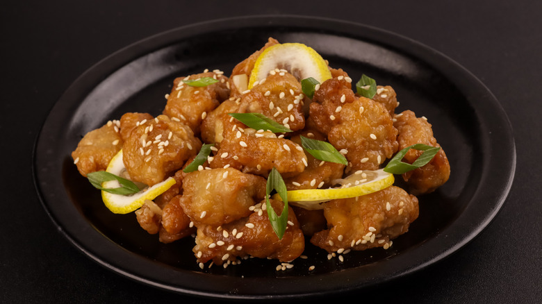 Crispy lemon chicken garnished with lemon wedges and spring onions.