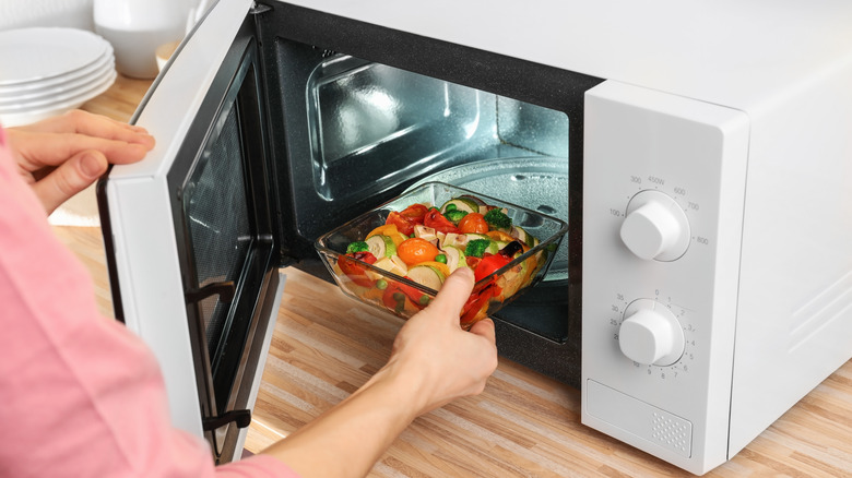 Hand placing vegetables in microwave