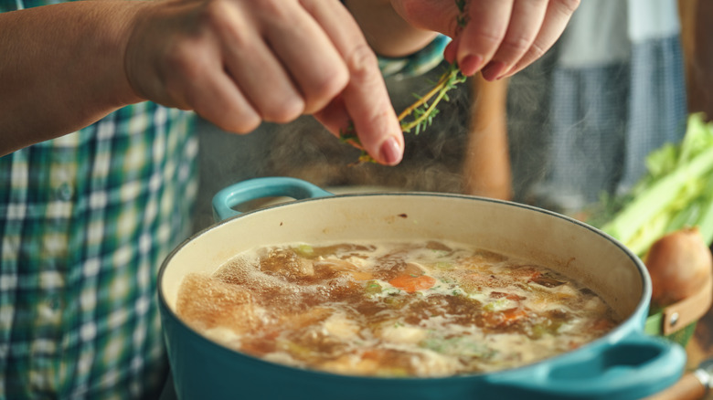 woman adding herbs to soup