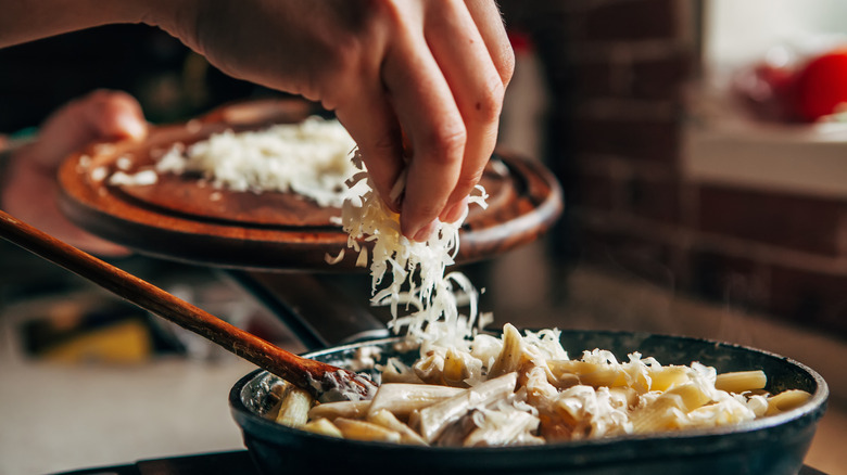 Cook adding shredded cheese to pasta