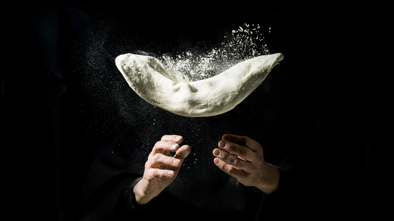 Two hands tossing pizza dough