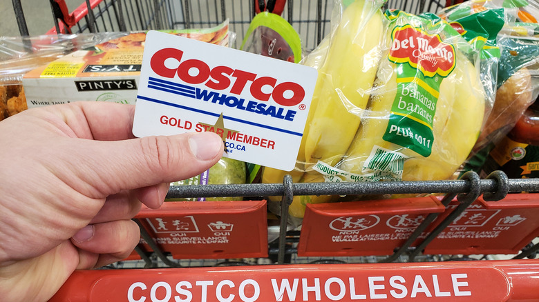 Hand holding costco membership card against grocery cart