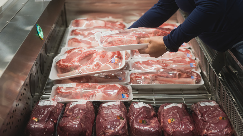 Person grabs meat from store fridge 