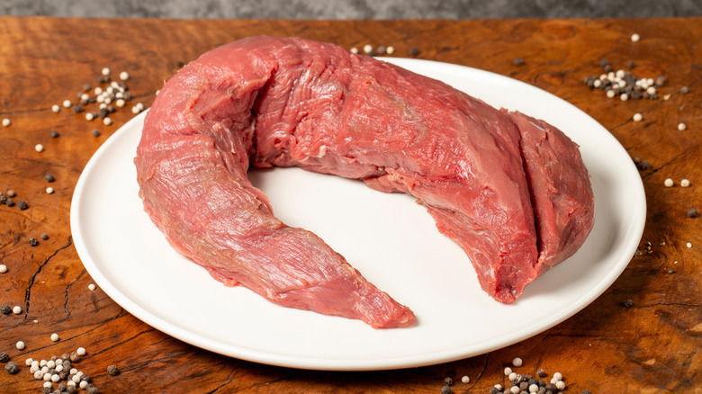 Raw, whole beef tenderloin on a white plate