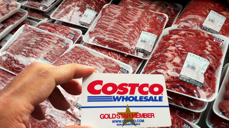 Person holding Costco membership card in front of refrigerated meat