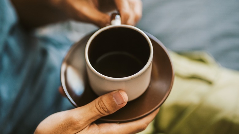 Hands hold a mug of coffee on a saucer