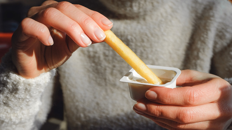 a woman dipping a french fry into a fast food container of unidentifiable dipping sauce