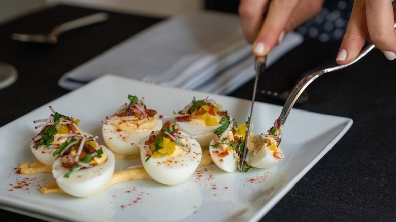 hands cutting deviled eggs with knife and fork