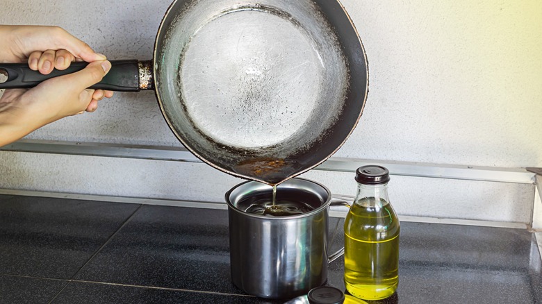 Hand pouring used cooking oil into cup