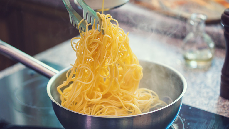 spaghetti noodles being cooked on a pan on the stove