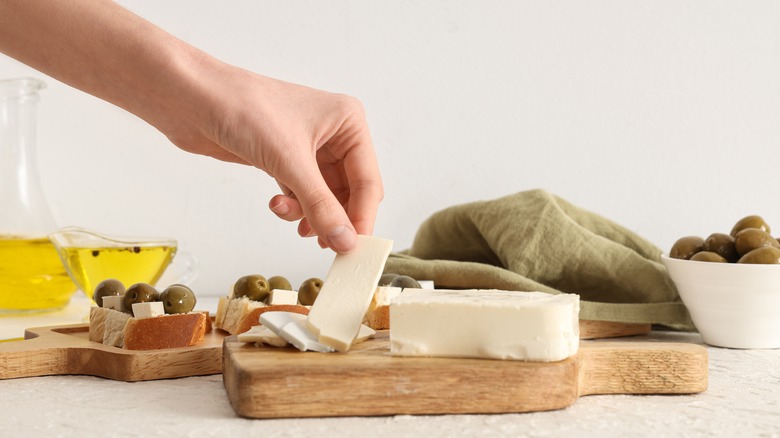 A hand touching feta cheese on a board