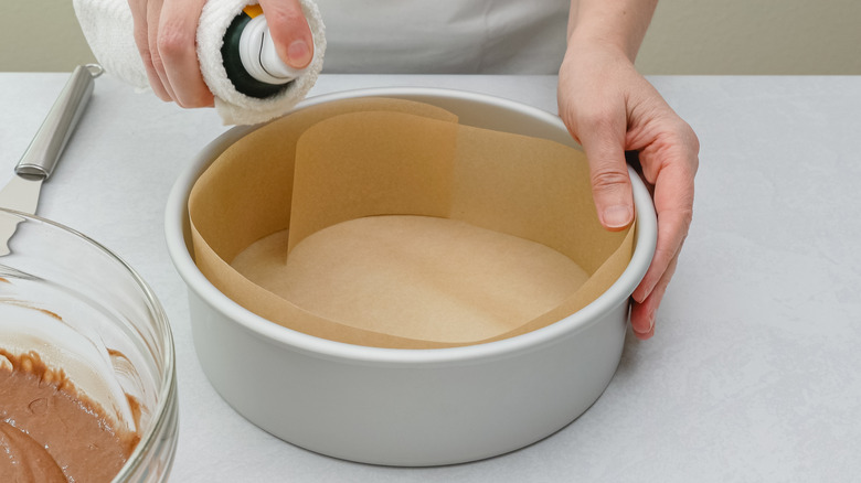 person spraying oil into circular cake pan