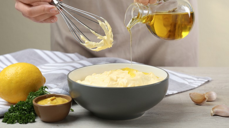 Whisking mayonnaise with oil with lemon and mustard on the side