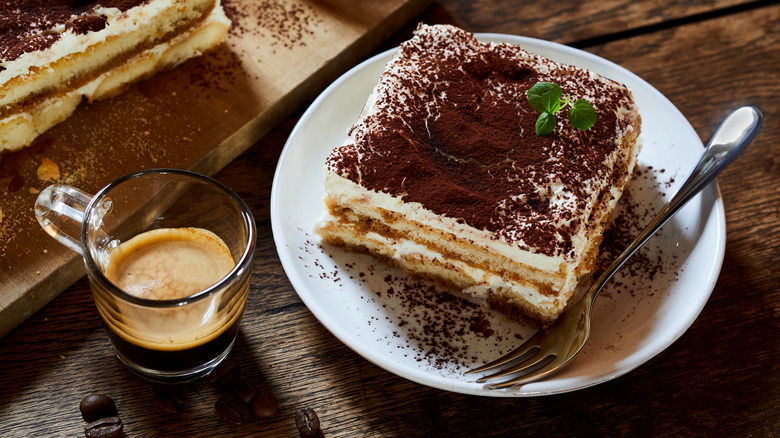 A shot of espresso beside a plate of tiramisu