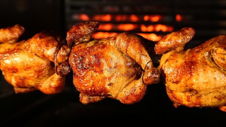 Three rotisserie chickens on spit in oven