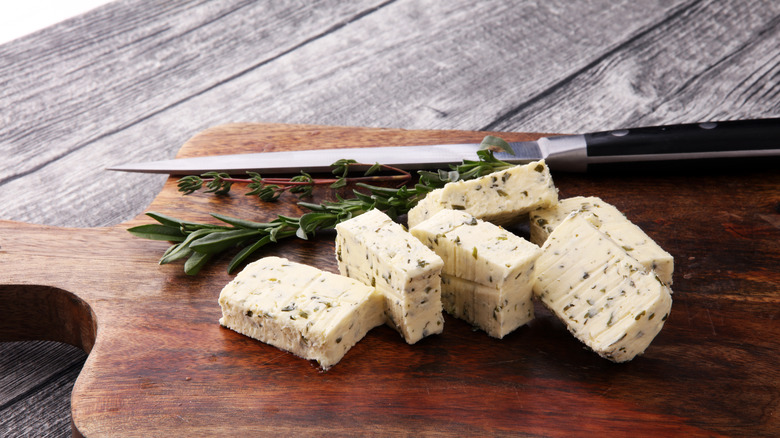 Blocks of compound butter on cutting board with herbs