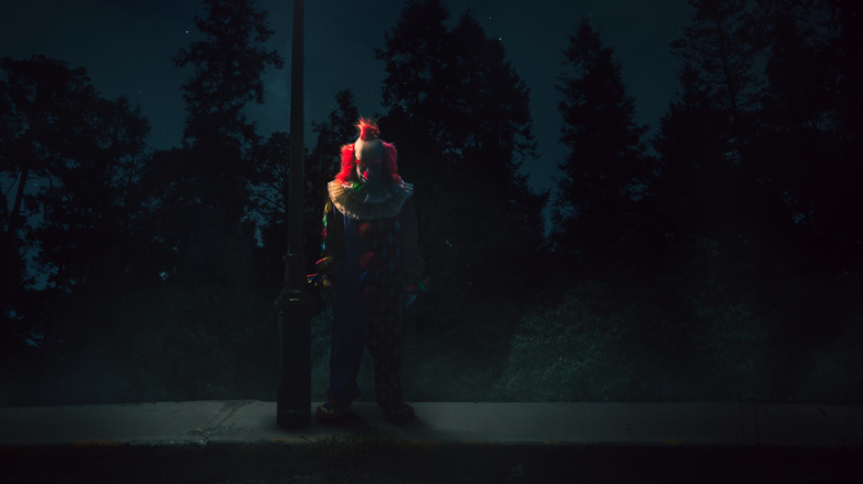 Scary clown standing by streetlamp