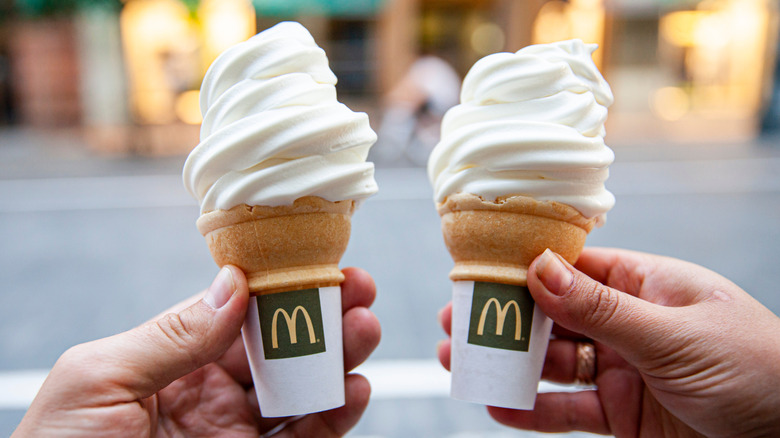 Hands hold up two vanilla McDonald's ice cream cones