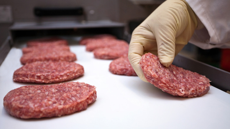 person laying ground beef burger patties on a baking sheet