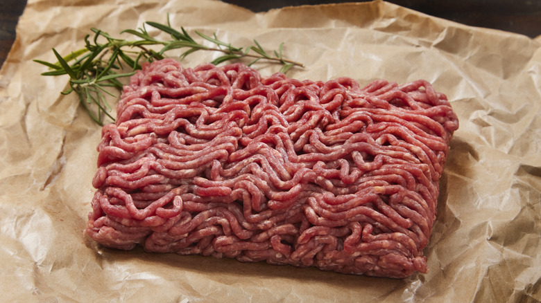 ground beef on parchment paper with a sprig of rosemary