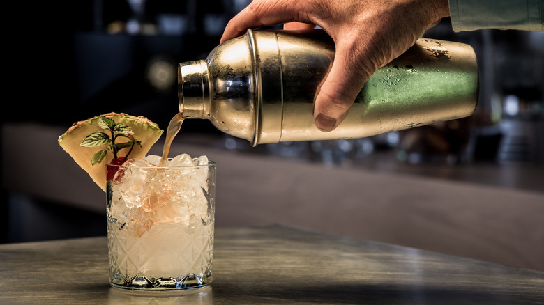 A hand pouring aa drink from a silver cocktail shaker