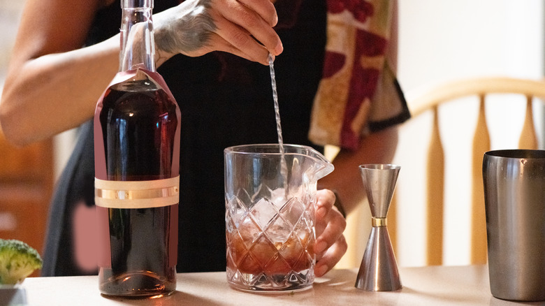 A person mixing a cocktail in a glass mixing glass