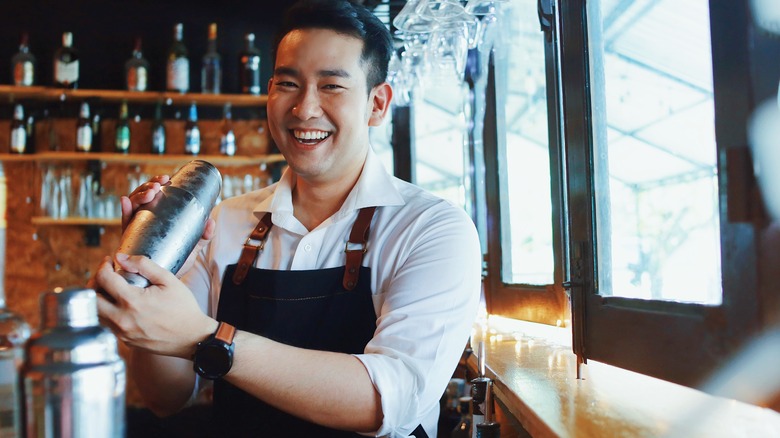 A man smiles while holding a cocktail shaker