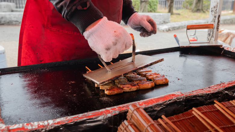 Person grill pressing chicken skewers