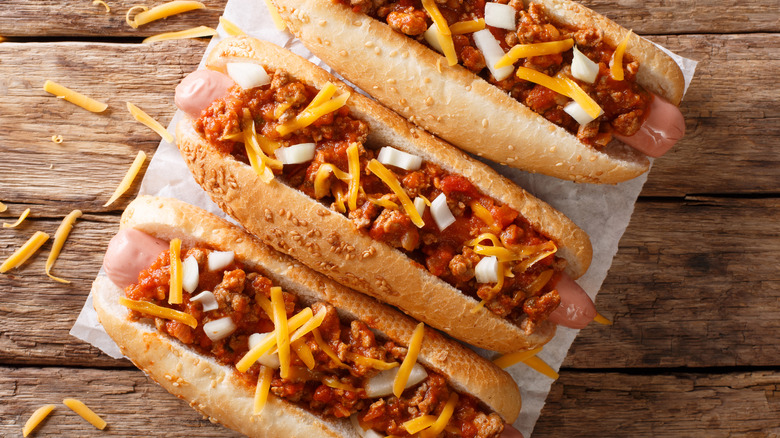 3 Chili dogs with cheese on a wooden board