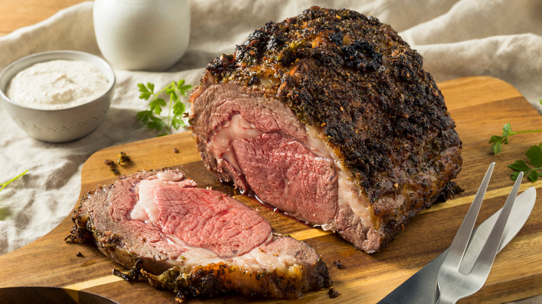 A cooked, boneless prime rib roast on a wooden carving board, cut open to show the fat