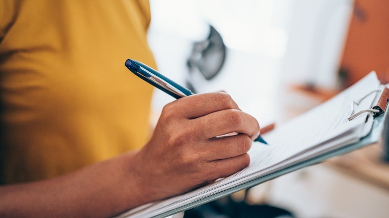 Closeup of woman writing notes on clipboard