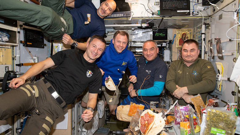 Astronauts at mealtime, with a half-made taco floating in the foreground