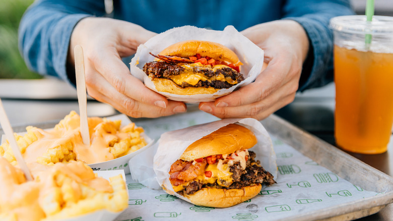 Hand holds burger over tray with more fast food.