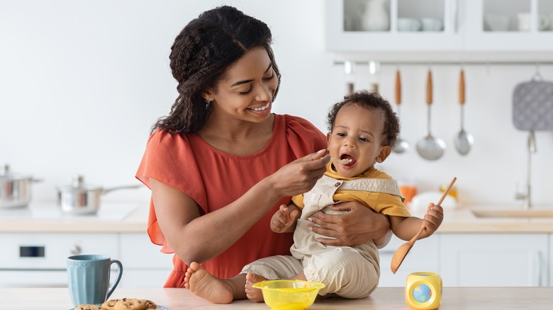 Mother feeding baby food in kitchen