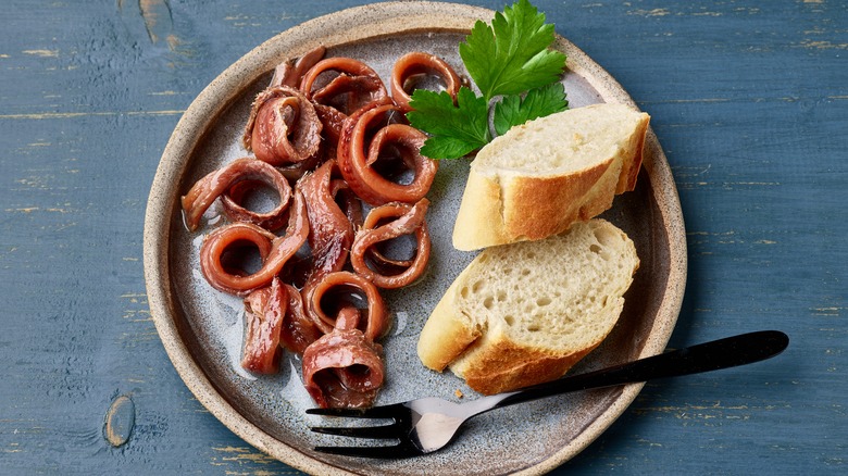 Anchovy filets curled on a plate next to bread