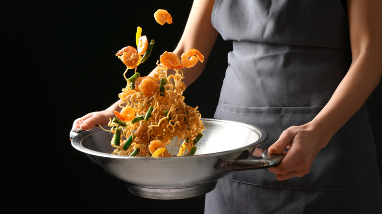 Person tossing food in a wok