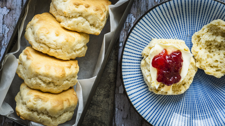 homemade fluffy scones with clotted cream and jam on a rustic wood table