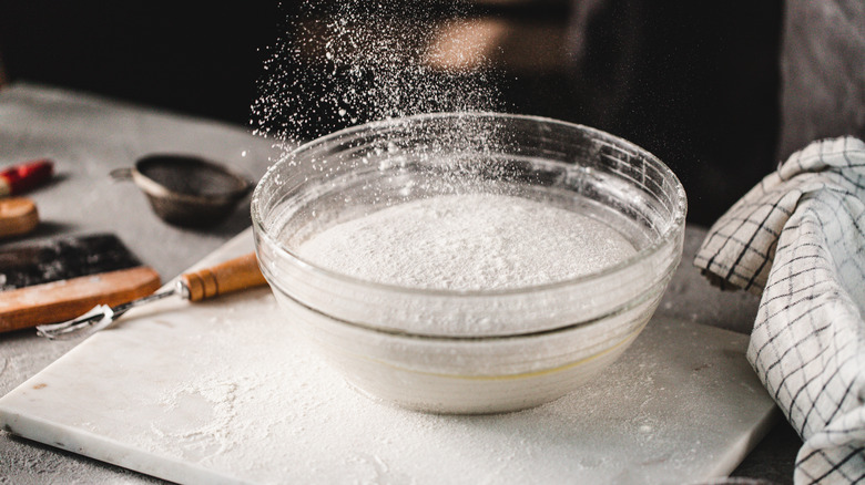 Bowl of flour on countertop with fragments of flour dusted in the air.