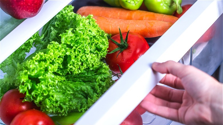 Hand near produce in refrigerator 