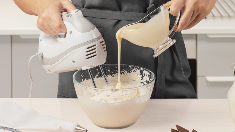 person making whipped cream in a glass bowl