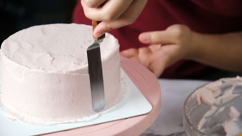 A person scraping the excess frosting