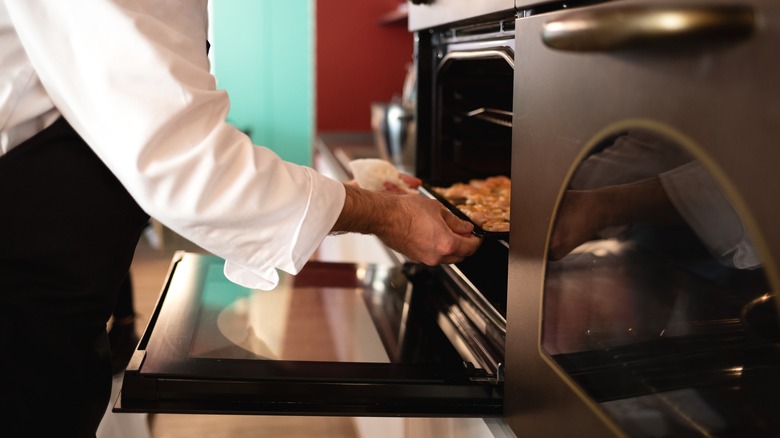 chef putting a tray of chicken fillets in an oven