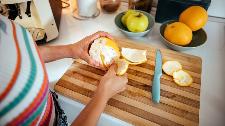 Hands peel an orange on cutting board