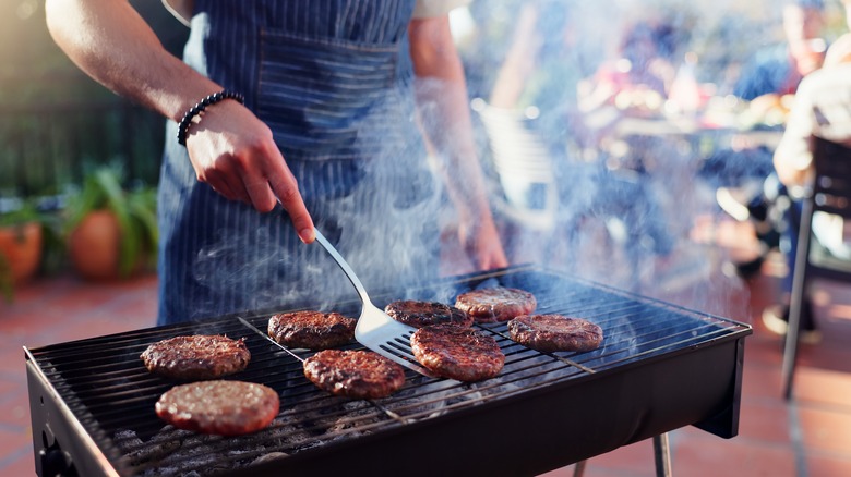 Person grilling several burger patties.